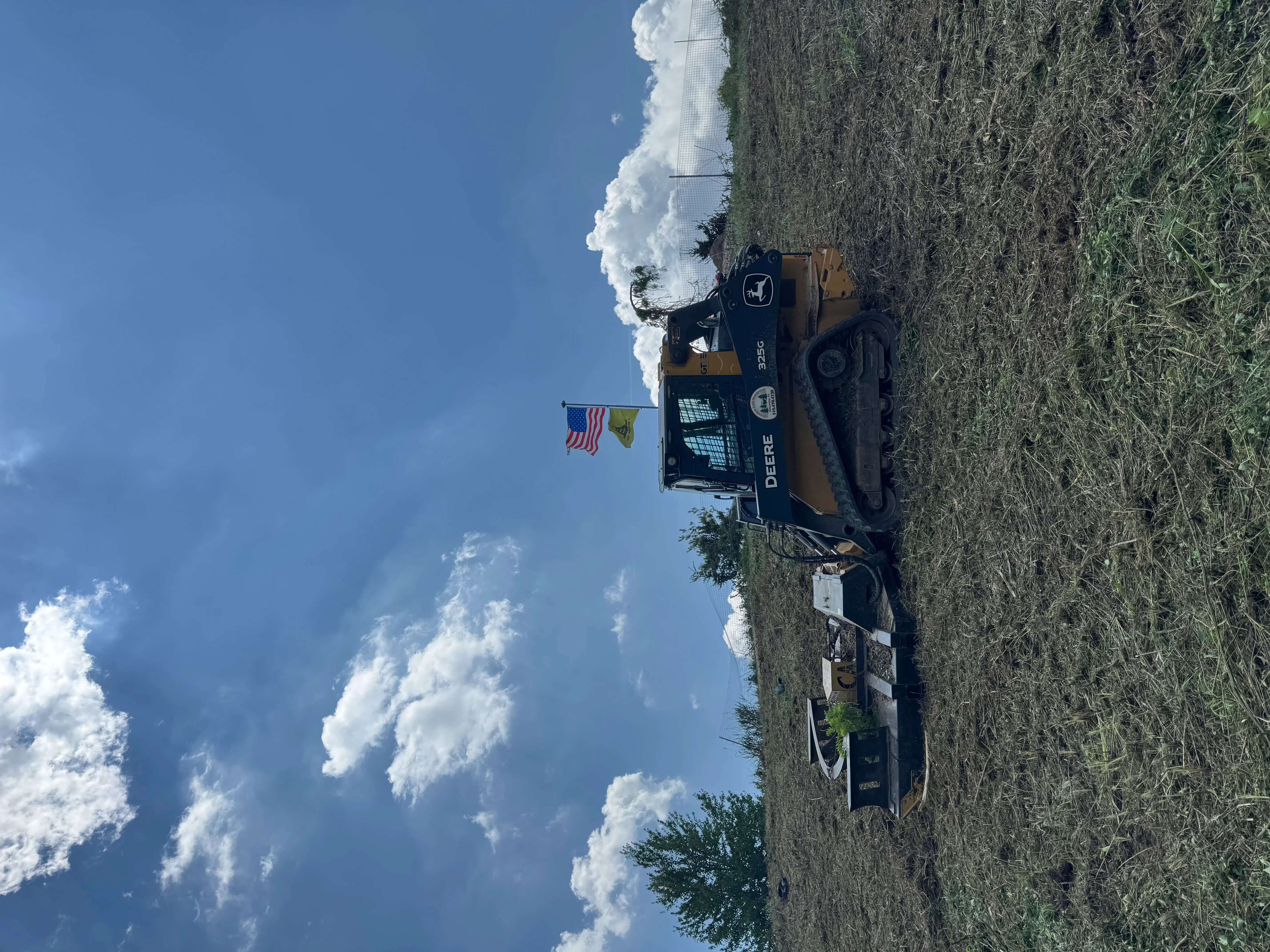 John Deere excavator with mulching attachment clearing overgrown brush and vegetation from rural acreage