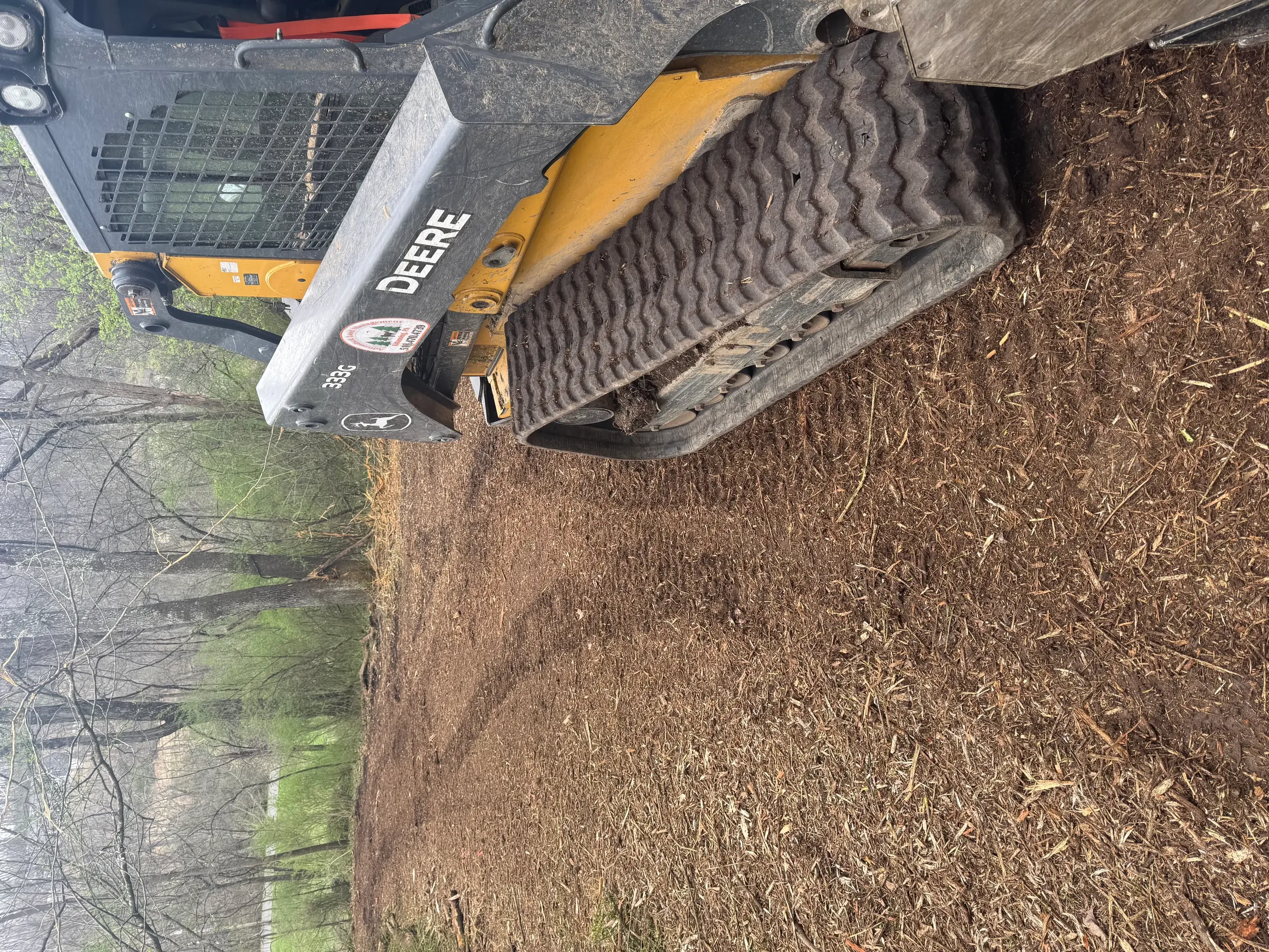 Yellow John Deere skid steer loader clearing overgrown vegetation and brush from property