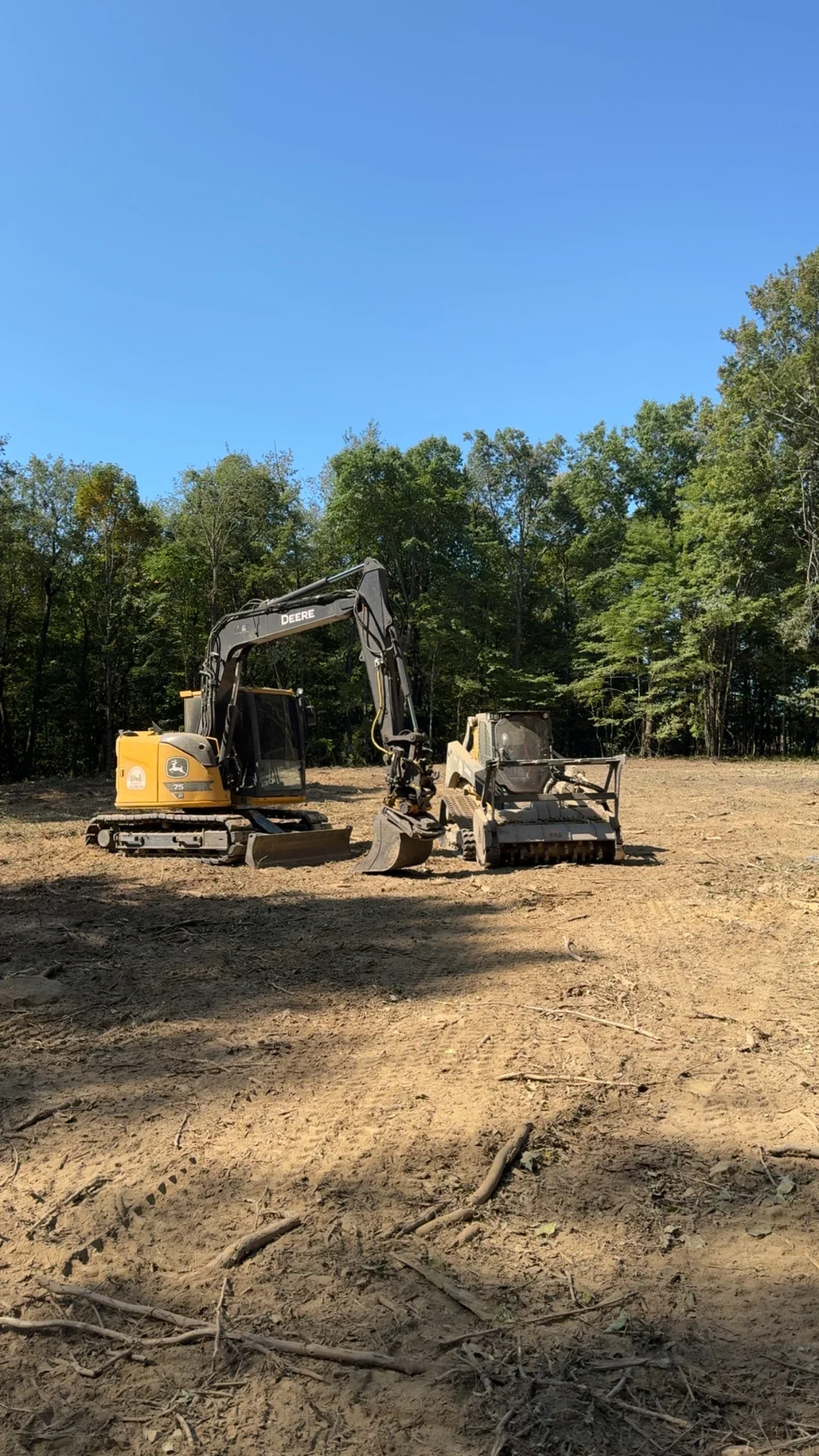 John Deere mini excavator clearing wooded lot with brush removal attachment