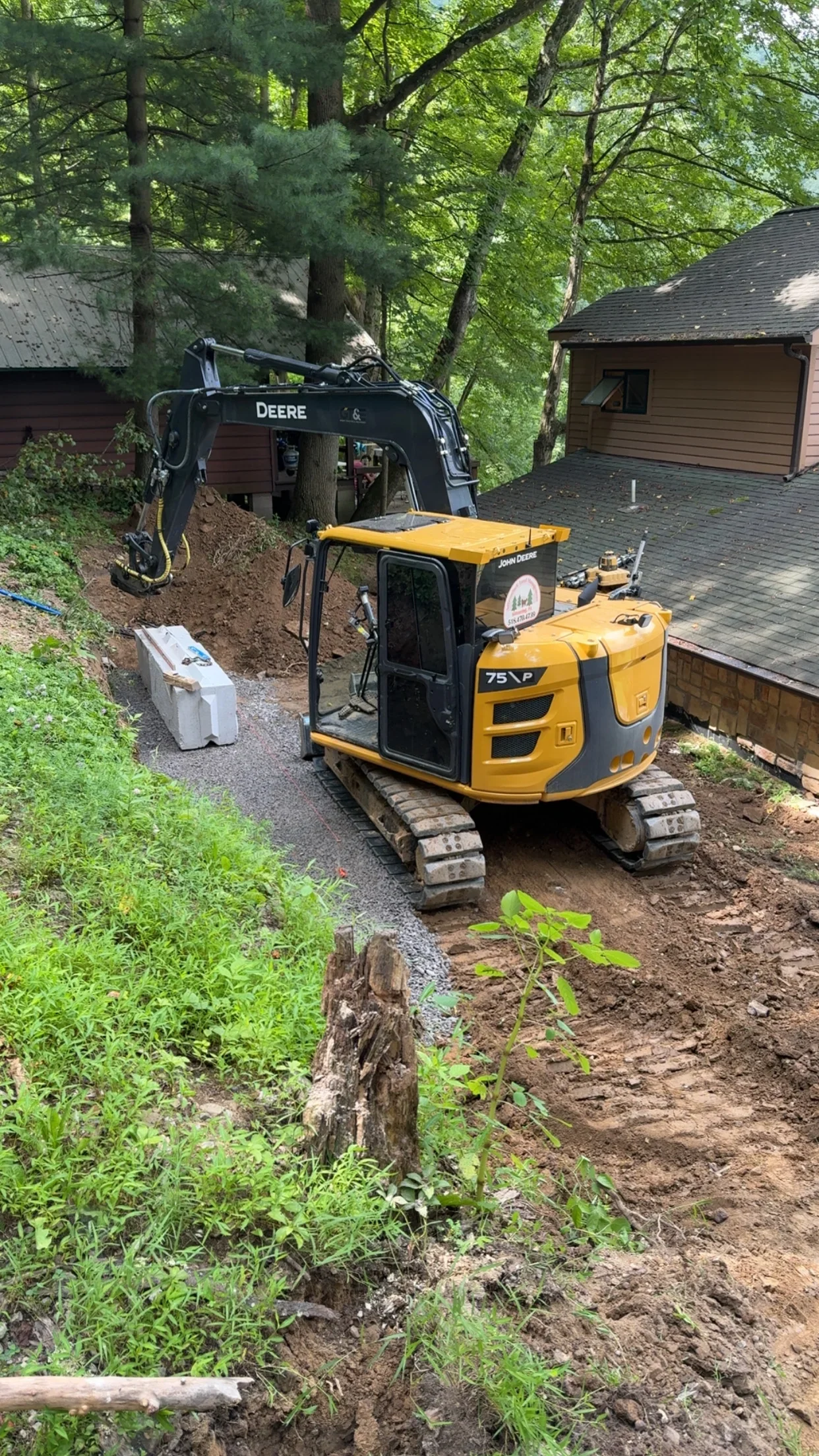 Yellow John Deere compact excavator working on residential lot excavation in wooded area